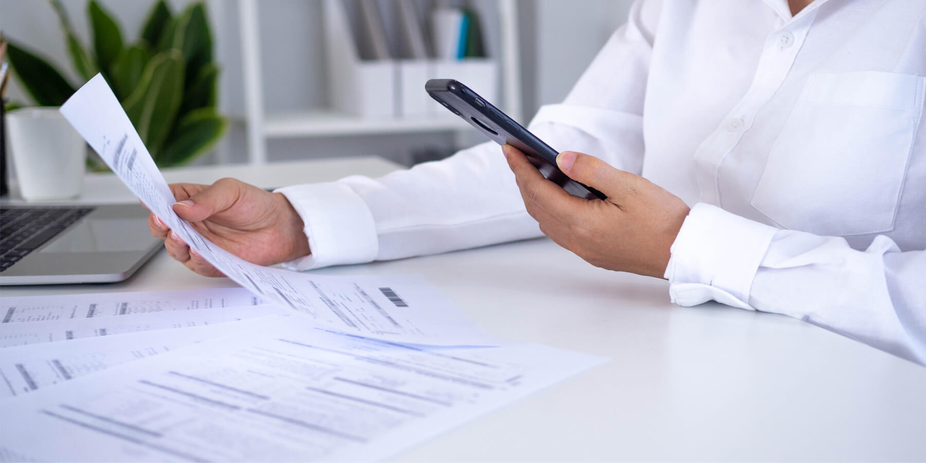 person in crisp white blouse looking at smart phone and printed document